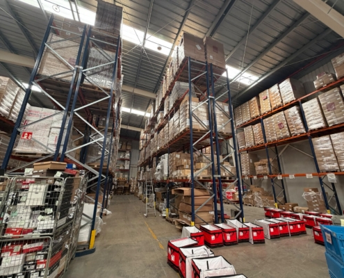Interior de una nave industrial con estanterías metálicas de gran altura y pasillos de almacenamiento para proyectos de CCTV y redes.